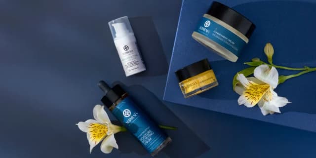 Four Nudmuses cosmetics arranged on a navy blue background accompanied by white flowers.