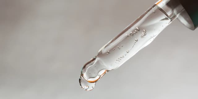Glass pipette with clear liquid on a gray background.