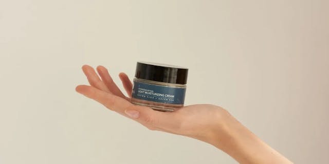 A light moisturizing cream by Nudmuses in a jar on an outstretched female hand