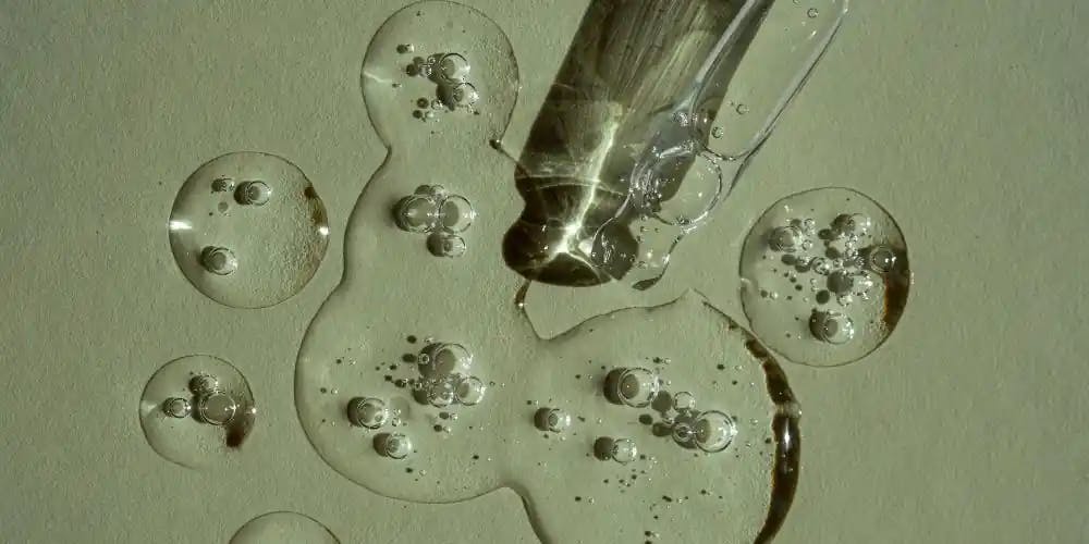 Przezroczyste serum rozlewające się ze szklanej pipety, na jasnozielone podłoże