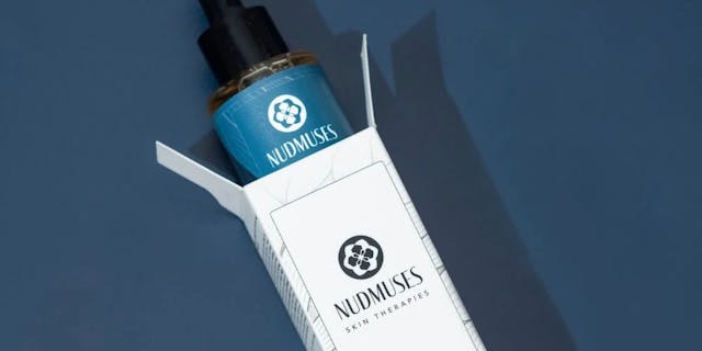 Nudmuses serum protruding from the packaging, lying on a navy blue background