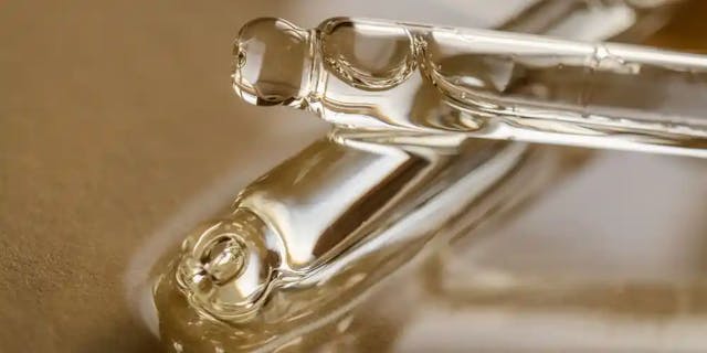 Przezroczysta szklan pipeta, która leży na złotym tle.
